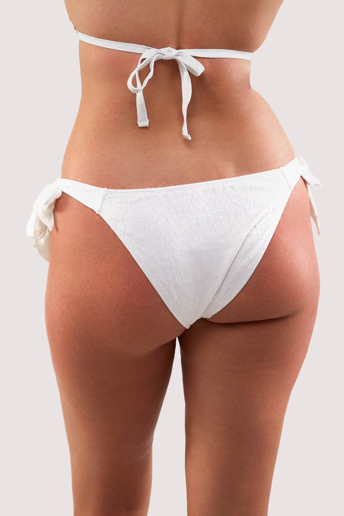 Model shows brief of white floral texture tie side bikini bottoms